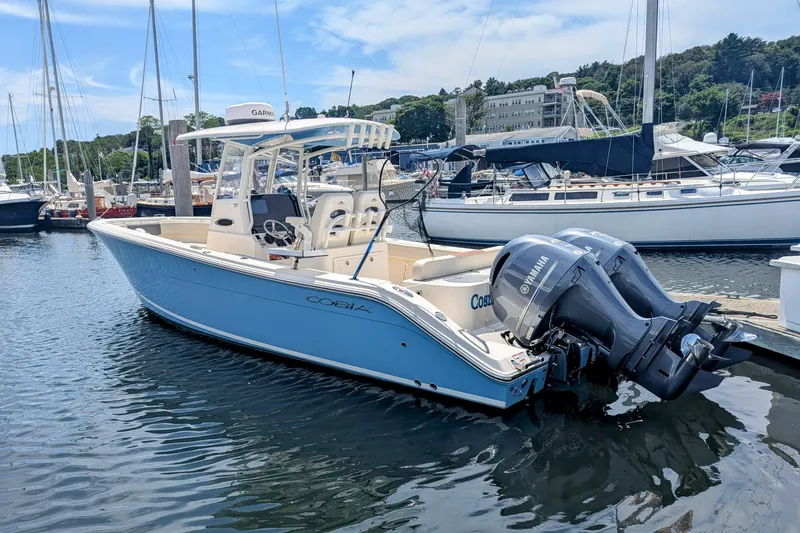 Slide: The Image of 2023 Cobia 280 Center Console boat docked in marina with twin Yamaha engines. - 1