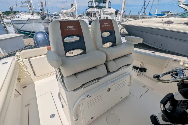 Slide: The Image of 2023 Cobia 280 Center Console boat interior with dual captain's chairs at a marina. - 11
