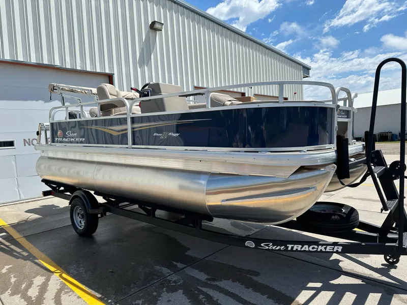 Slide: The Image of 2025 Sun Tracker Bass Buggy 18 DLX pontoon boat on trailer, parked outdoors. - 3