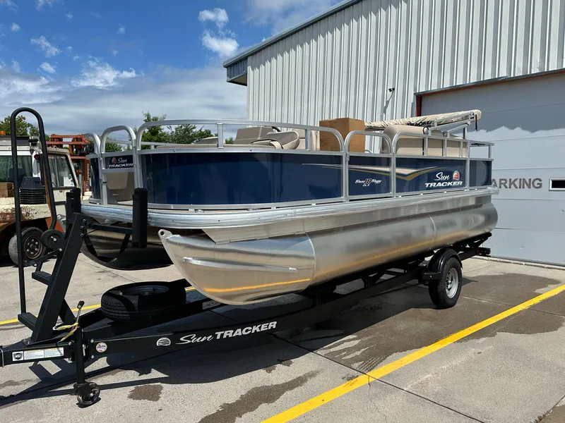 Slide: The Image of 2025 Sun Tracker Bass Buggy 18 DLX pontoon boat on trailer, parked outdoors. - 4