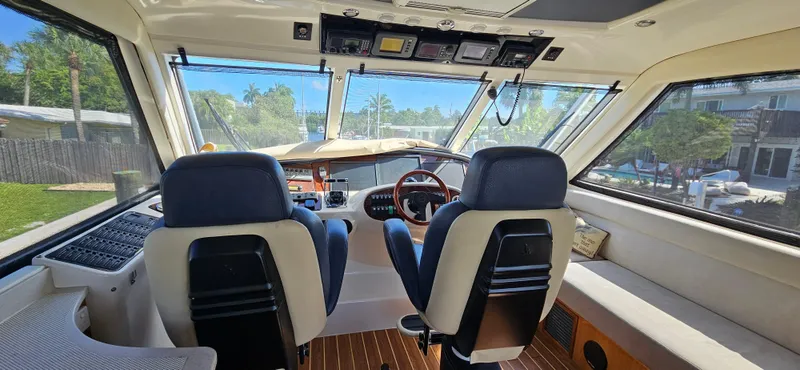 Slide: The Image of Interior view of 2004 Riviera 58 Enclosed Flybridge yacht cockpit with dual seats and panoramic windows. - 28
