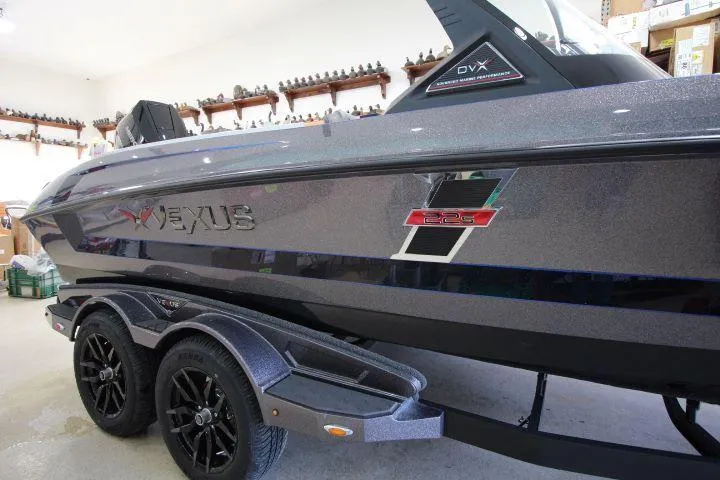 Slide: The Image of 2025 Vexus DVX22S boat in showroom, sleek design with dual-axle trailer. - 2