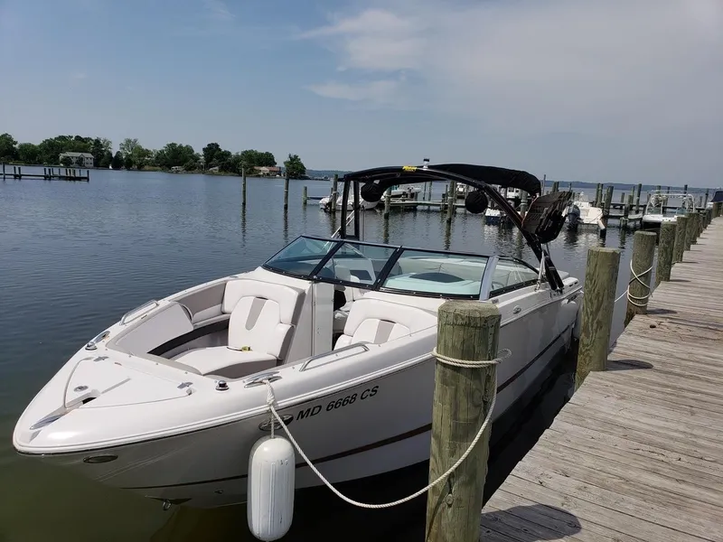 The Image of 2017 Four Winns H260 boat on trailer, parked outdoors near trees and houses. - 0