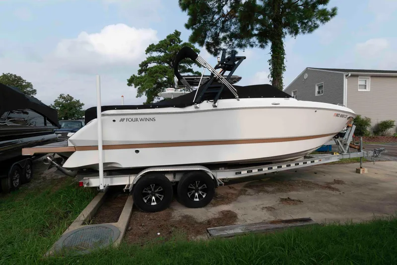 Slide: The Image of 2017 Four Winns H260 boat on trailer, parked outdoors near trees and houses. - 2