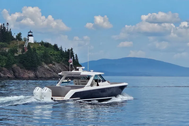 Slide: The Image of 2024 Tiara Yachts 43 LS cruising near a scenic lighthouse and forested coastline. - 2