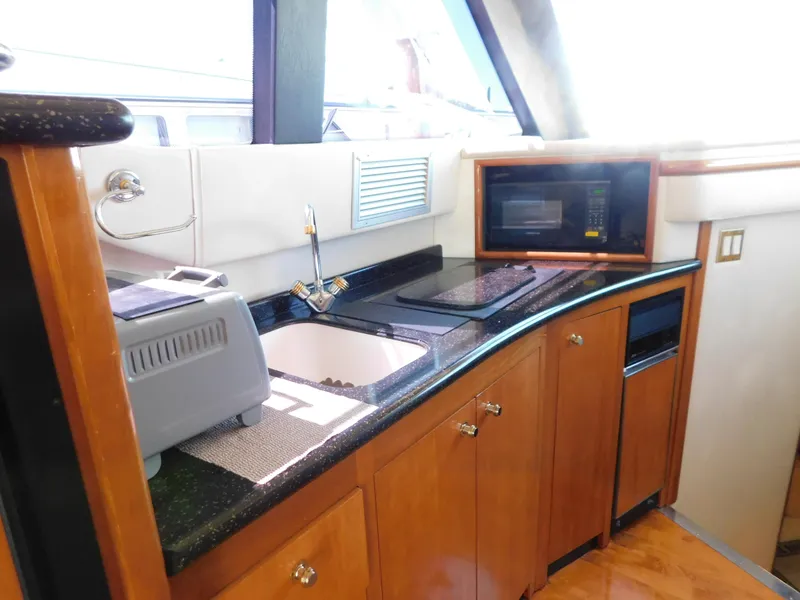 Slide: The Image of 2002 Carver 450 Voyager Pilothouse kitchen with sink, microwave, and wooden cabinetry. - 21
