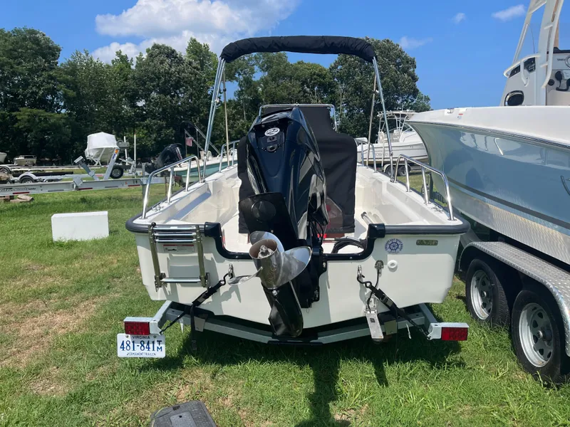 Slide: The Image of 2025 Boston Whaler 150 Montauk boat on trailer, parked on grass, with outboard motor. - 18
