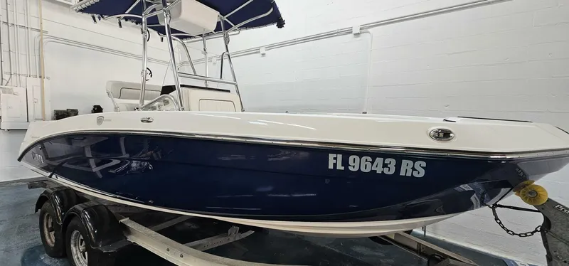 The Image of 2018 Yamaha Boats 210 FSH Deluxe, blue and white, on trailer in indoor storage. - 0