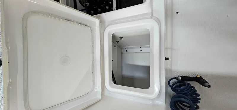 Slide: The Image of Open storage compartment on 2018 Yamaha Boats 210 FSH Deluxe with coiled hose. - 26