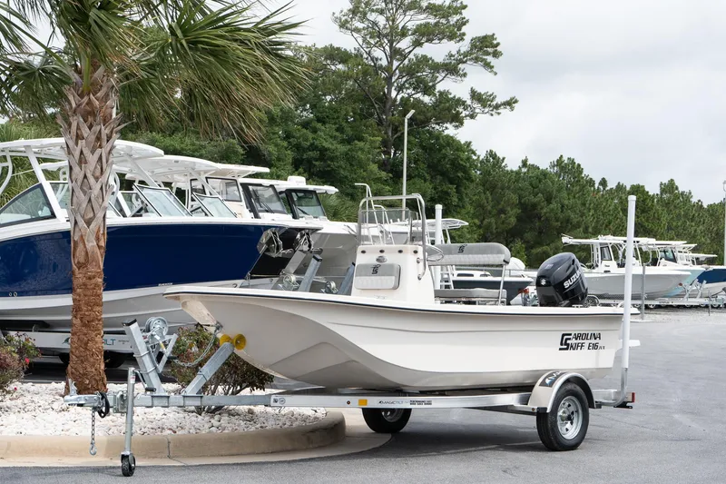 Slide: The Image of 2025 Carolina Skiff E16 JVX CC boat on trailer, parked near palm tree. - 2