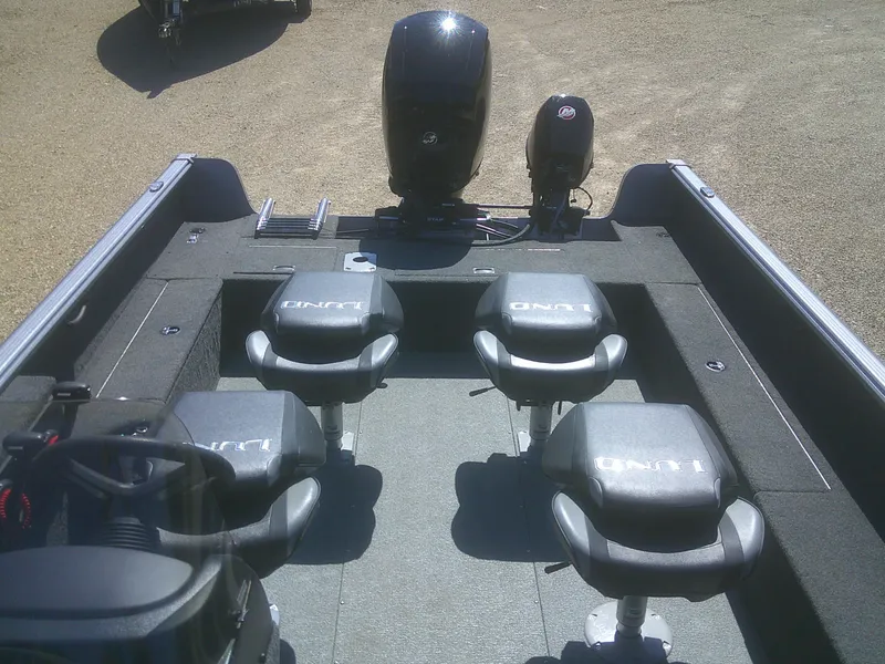 Slide: The Image of 2020 Lund 1875 Impact SS boat interior with seating and motor, on a sandy surface. - 12