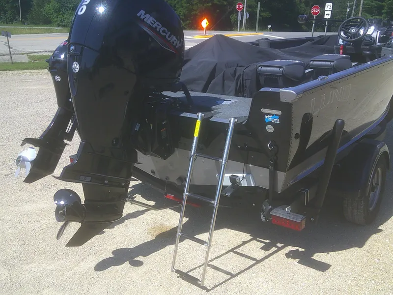 Slide: The Image of 2020 Lund 1875 Impact SS boat with Mercury outboard motor and ladder, parked on gravel. - 16