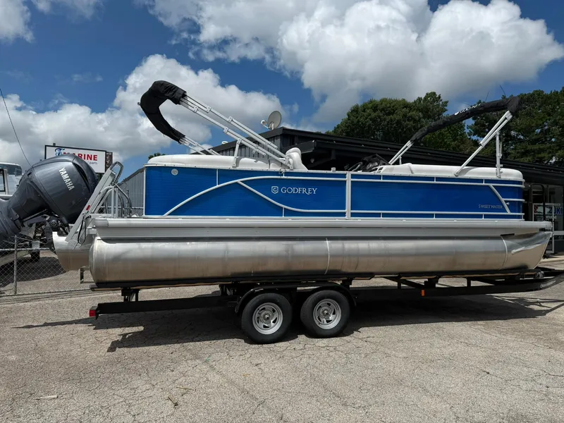Slide: The Image of 2024 Godfrey SWEETWATER 2286 SB pontoon boat on trailer, blue and silver design. - 2