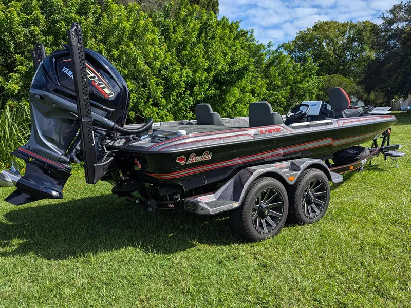The Image of 2026 Bass Cat Lynx STS boat on trailer, parked on grass with lush greenery background. - 0