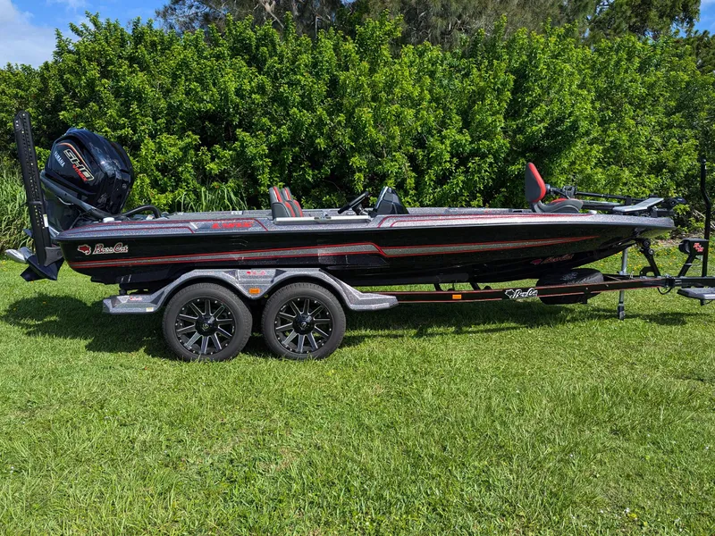 Slide: The Image of 2026 Bass Cat Lynx STS boat on trailer, parked on grass with lush greenery background. - 2