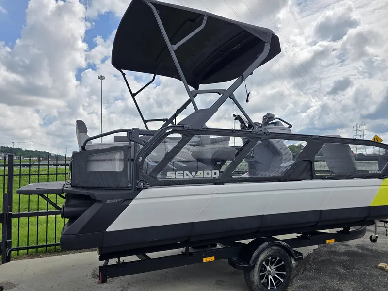 Slide: The Image of 2023 Sea-Doo Switch Sport 21 pontoon boat with canopy, parked outdoors under cloudy sky. - 2
