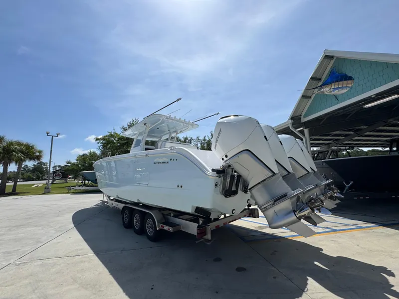 Slide: The Image of 2026 Invincible 38 Catamaran with triple outboard engines on trailer, under clear blue sky. - 16