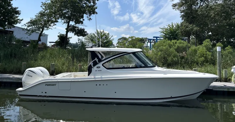 Slide: The Image of 2026 Pursuit DC 306 boat docked by lush greenery under a clear sky. - 0