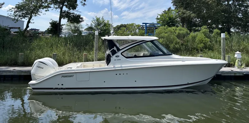 Slide: The Image of 2026 Pursuit DC 306 boat docked by lush greenery under a clear sky. - 1