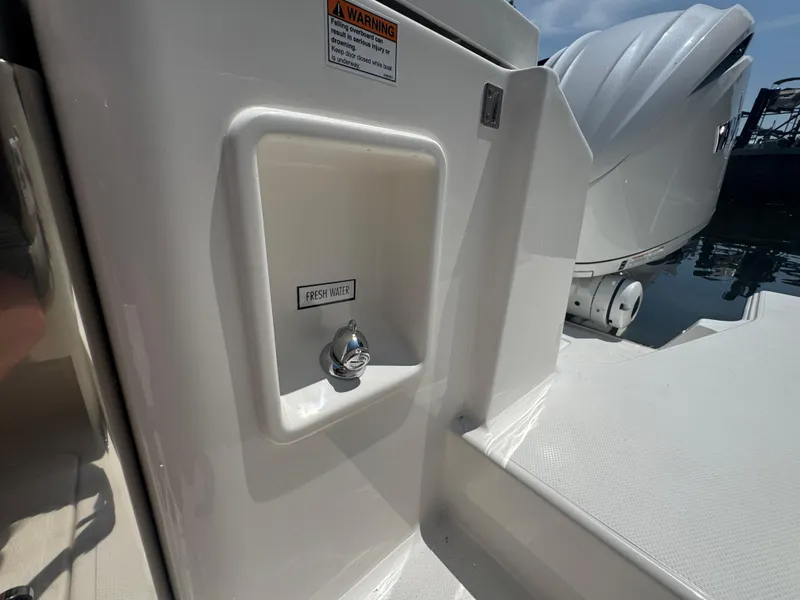 Slide: The Image of Freshwater outlet on 2026 Pursuit DC 306 boat, near engine, with warning label. - 10