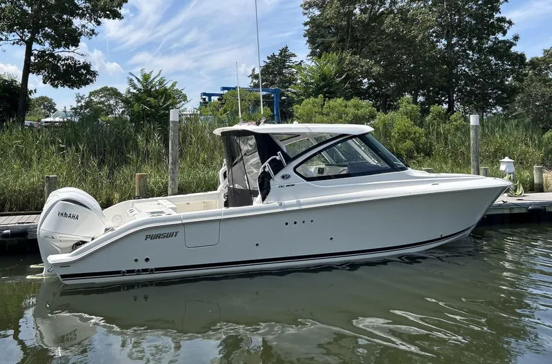 Slide: The Image of 2026 Pursuit DC 306 boat docked on calm water, surrounded by lush greenery. - 2