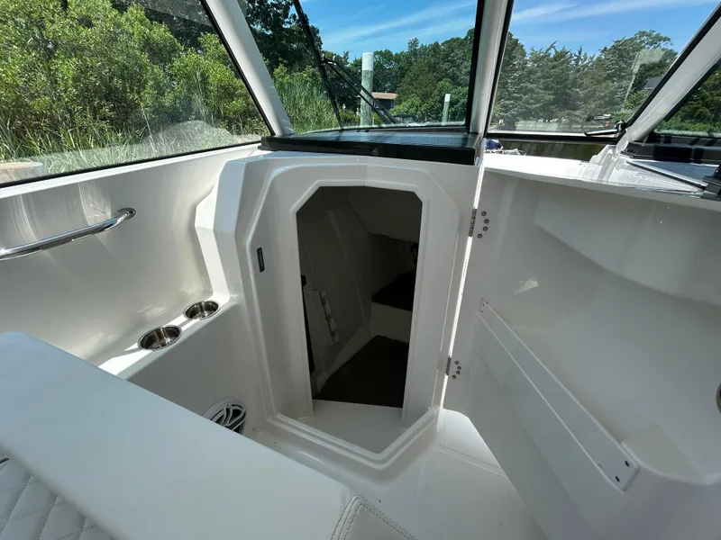 Slide: The Image of 2026 Pursuit DC 306 boat interior with open cabin door, sleek white design, and cup holders. - 30
