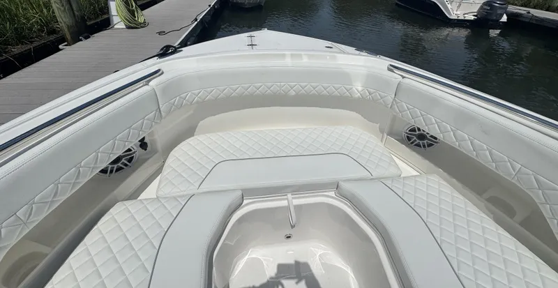 Slide: The Image of 2026 Pursuit DC 306 boat interior with white quilted seating and speakers, docked by the water. - 34