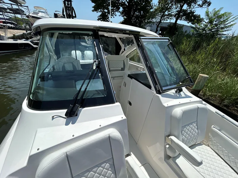 Slide: The Image of 2026 Pursuit DC 306 boat with white seating and windshield, docked near greenery. - 39