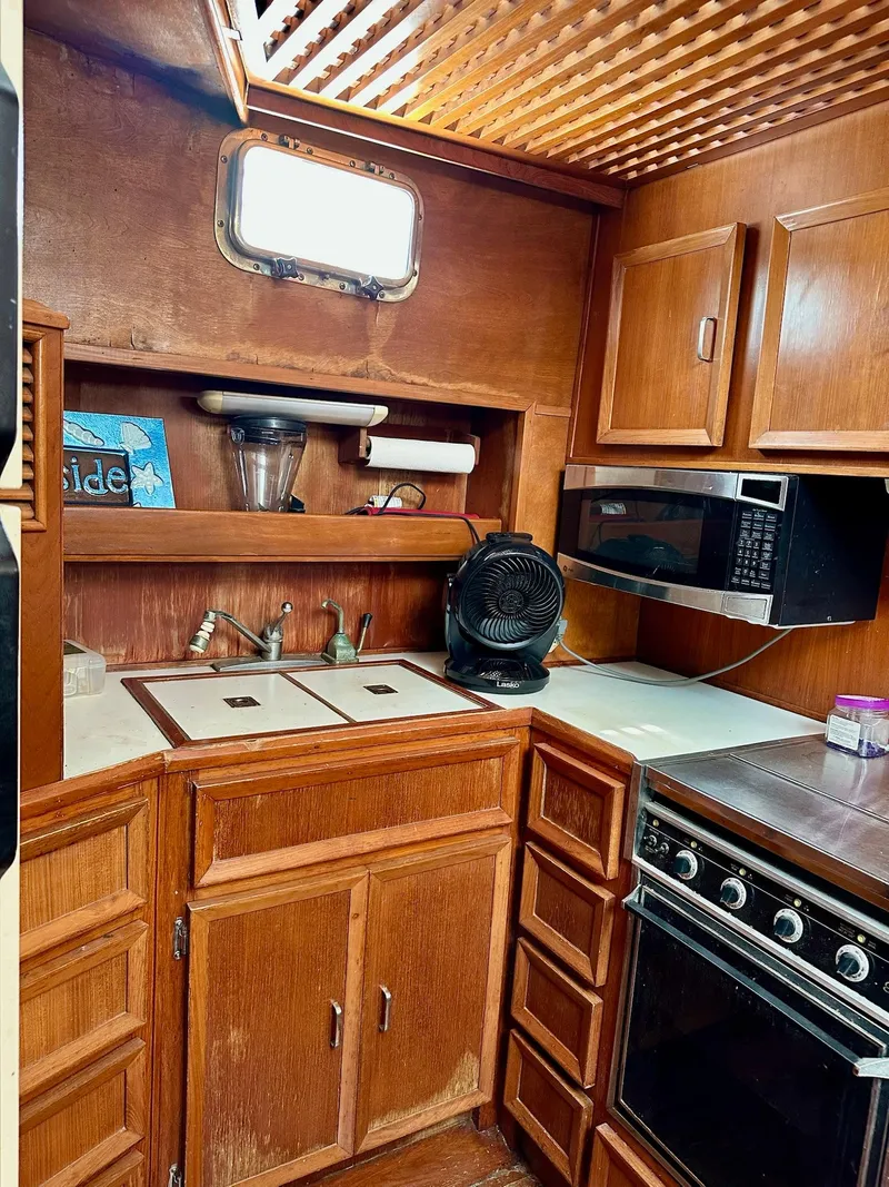 Slide: The Image of 1987 Jefferson Sundeck boat kitchen with wooden cabinets, sink, microwave, and stove. - 22