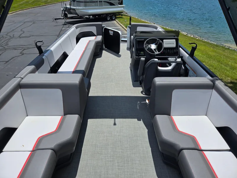 Slide: The Image of 2024 Manitou Cruise pontoon boat interior with modern seating and steering console by the water. - 15