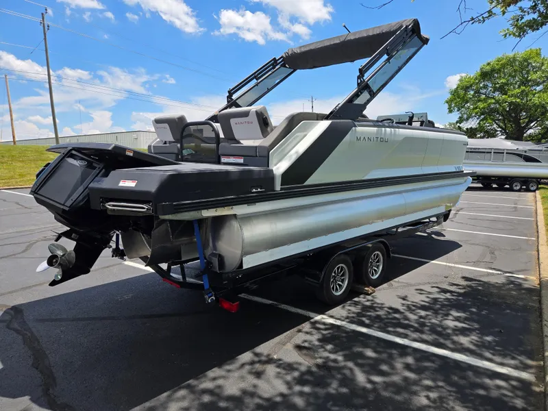 Slide: The Image of 2024 Manitou Cruise pontoon boat on trailer in parking lot under blue sky. - 3