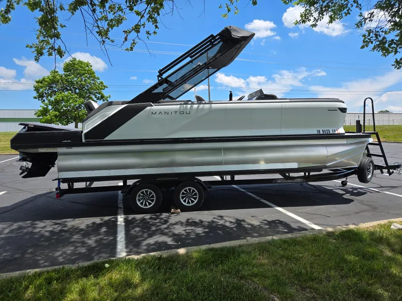 Slide: The Image of 2024 Manitou Cruise pontoon boat on trailer in parking lot, under clear blue sky. - 4