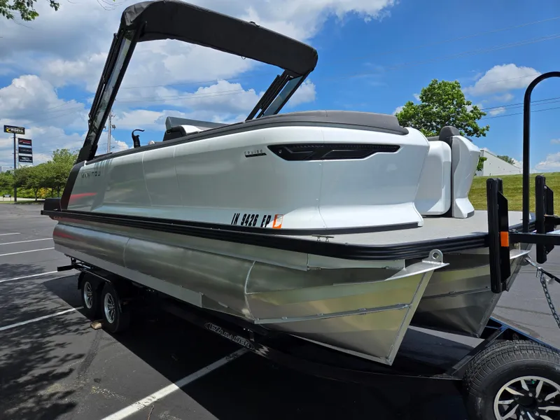 Slide: The Image of 2024 Manitou Cruise pontoon boat on trailer in parking lot under blue sky. - 5