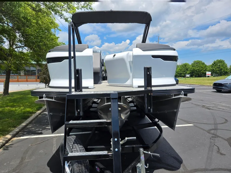 Slide: The Image of 2024 Manitou Cruise pontoon boat on trailer, parked outdoors under a blue sky. - 6