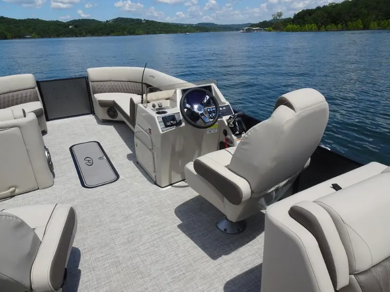 Slide: The Image of 2023 Harris Sunliner 250 pontoon boat interior with plush seating on a scenic lake. - 12