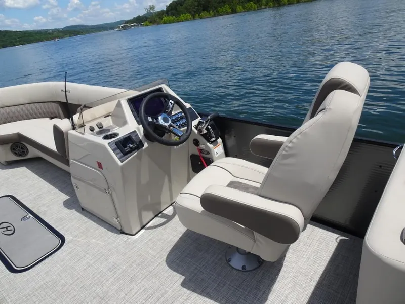 Slide: The Image of 2023 Harris Sunliner 250 boat interior with steering console and comfortable seating on a lake. - 13