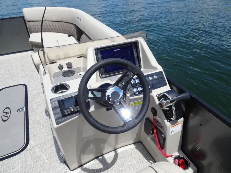 Slide: The Image of 2023 Harris Sunliner 250 boat helm with steering wheel and control panel on water. - 14