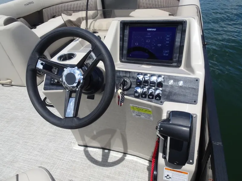 Slide: The Image of 2023 Harris Sunliner 250 boat dashboard with steering wheel and control panel on water. - 16
