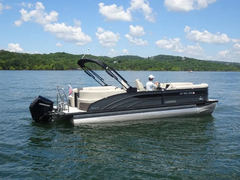 Slide: The Image of 2023 Harris Sunliner 250 pontoon boat cruising on a lake under a clear blue sky. - 2