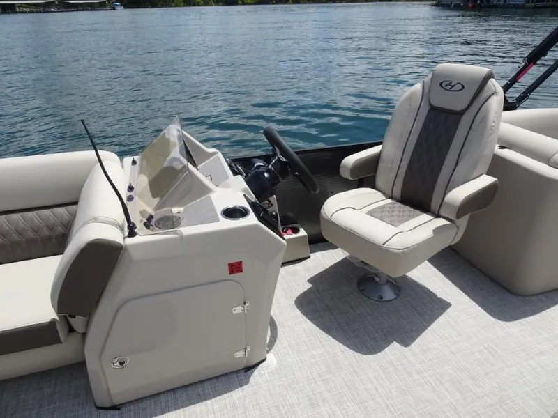 Slide: The Image of 2023 Harris Sunliner 250 boat interior with captain's chair and steering console on a lake. - 24