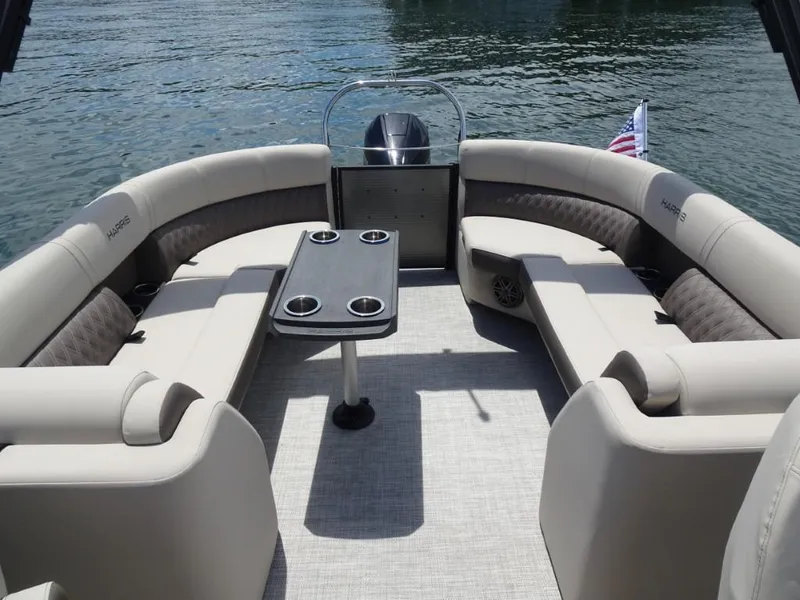 Slide: The Image of 2023 Harris Sunliner 250 pontoon boat interior with plush seating and table on the water. - 25