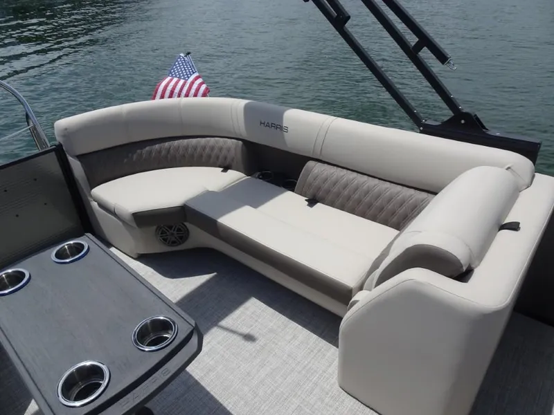 Slide: The Image of 2023 Harris Sunliner 250 boat interior with plush seating and American flag on water. - 27