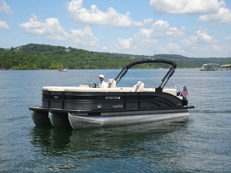 Slide: The Image of 2023 Harris Sunliner 250 pontoon boat cruising on a scenic lake under a blue sky. - 7