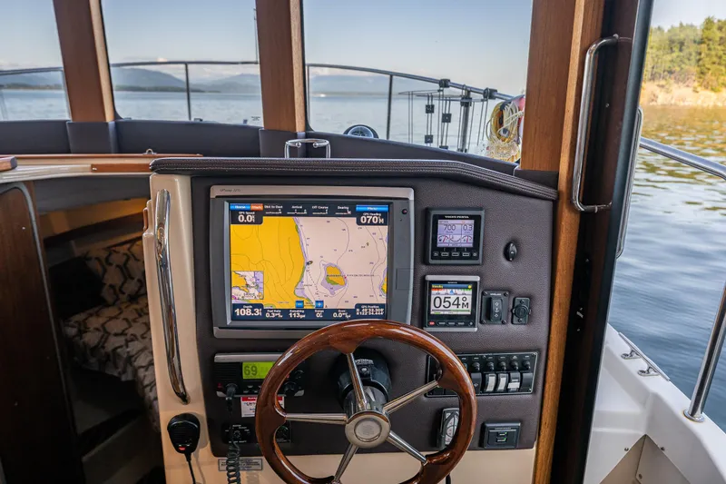 Slide: The Image of 2014 Ranger Tugs R-31CB helm with navigation display and steering wheel on calm water. - 21