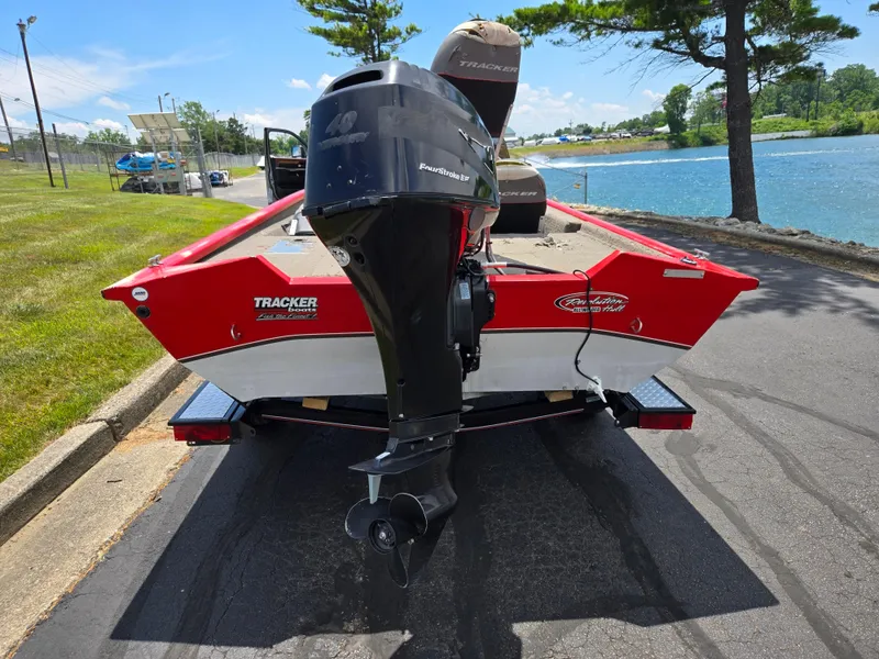 Slide: The Image of 2004 Tracker Pro Team 175 boat with outboard motor, parked near a lake on a sunny day. - 2