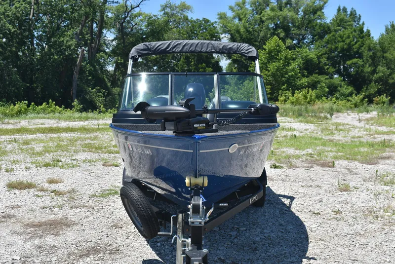 Slide: The Image of 2022 Lund 1650 Angler Sport boat on trailer, parked on gravel with trees in background. - 2
