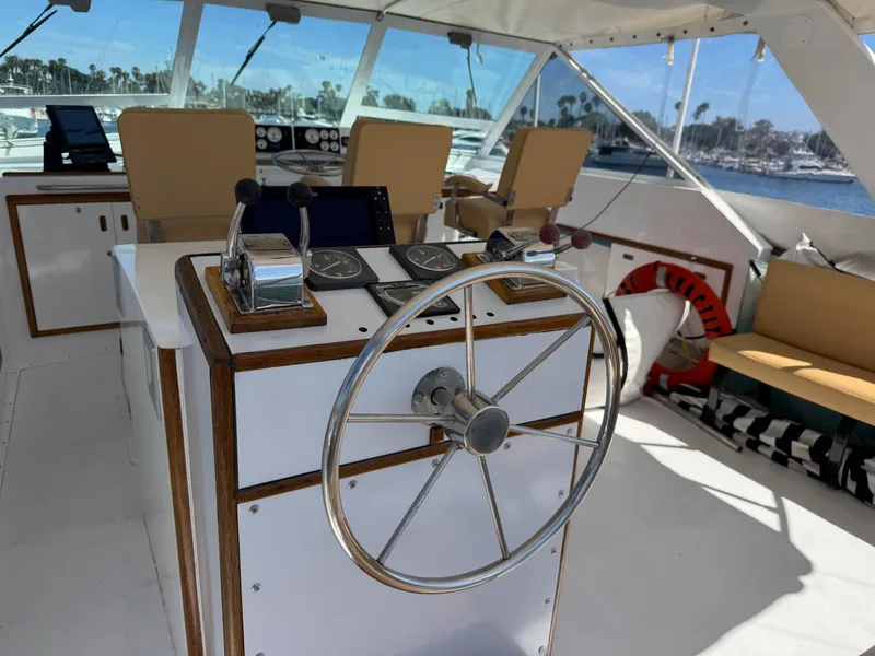 Slide: The Image of 1981 Bertram 58 Flybridge Motor Yacht helm with steering wheel and controls, overlooking marina. - 32