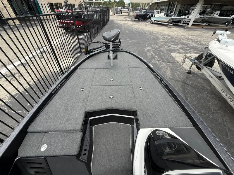 Slide: The Image of 2022 Skeeter ZX 150 boat deck with seating and storage, parked near a fence. - 26