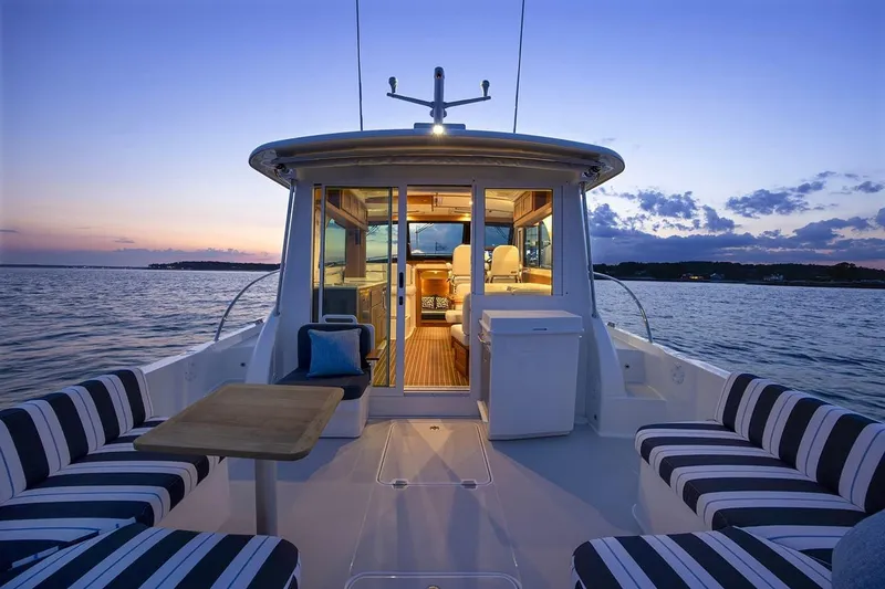Slide: The Image of 2026 Back Cove 412 yacht interior at sunset, featuring striped seating and a wooden table. - 7