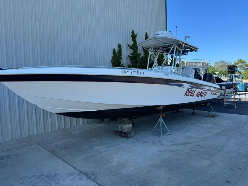 Slide: The Image of 1998 Wellcraft Scarab Sport 302 boat on stands, labeled "Reel Nauti," near a metal building. - 1